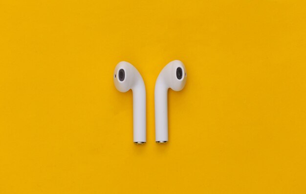 Modern wireless earphones on yellow background.