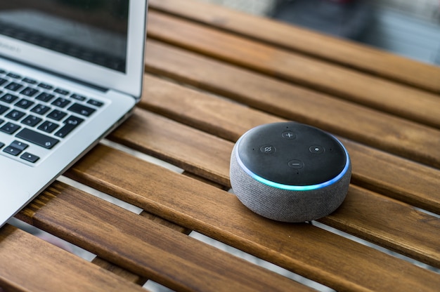 Photo modern wireless smart speaker placed on wooden table near blurred laptop at home