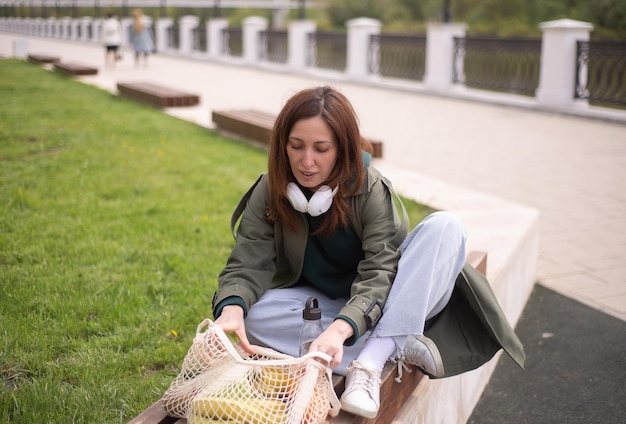 a modern woman is sitting on the street bench and taking products from packet