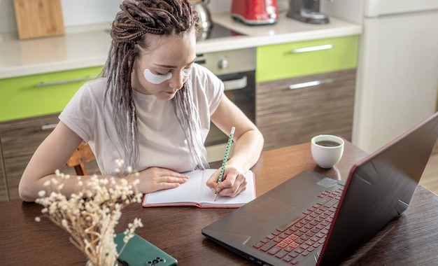 Photo modern woman with cosmetic eye mask on her face is working at home using a laptop