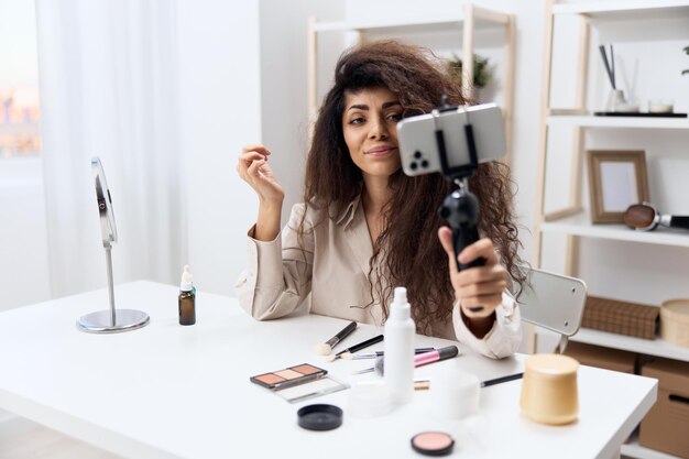 Modern work enjoyed tanned handsome curly latin beauty blogger\
in linen shirt sit on chair in home white interior copy space\
mockup banner influencer record video review blog using\
smartphone