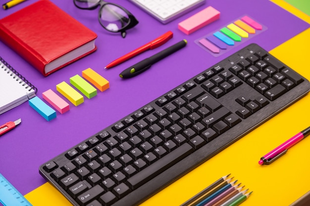 Modern working place with keyboard, diary, pencils, pens and glasses on orange-purple.