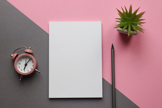 Modern workplace with notepad, pencil, plant, and alarm clock