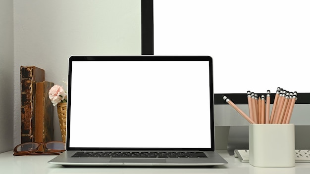 Modern workspace with a blank screen laptop, pencils and book on white table