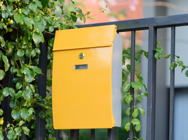 Modern yellow mail box on black fence with beautiful yellows background