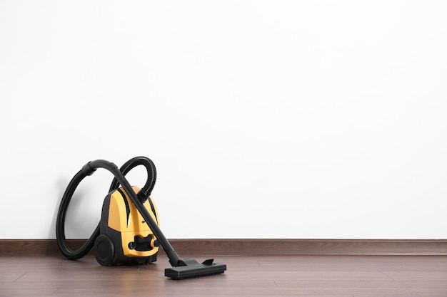 Modern yellow vacuum cleaner on wooden floor near white wall space for text