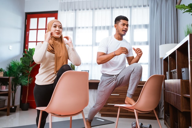 Modern young asian couple exercising at home using chair to help them workout