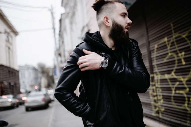 Modern young bearded man in black style clothes is walking at street.