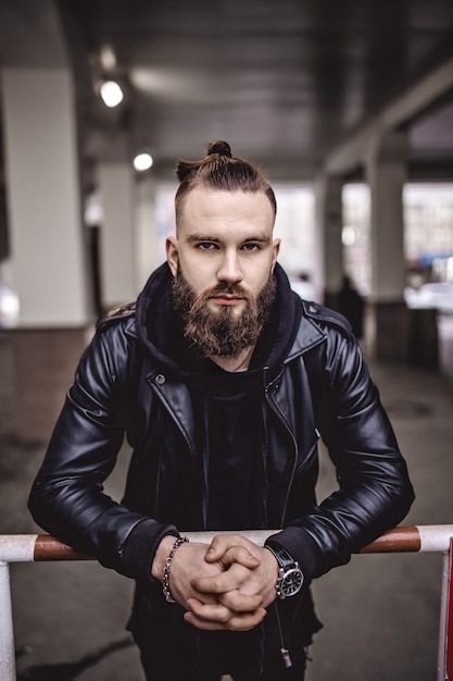 Modern young bearded man in black style clothes standing in around urban background.