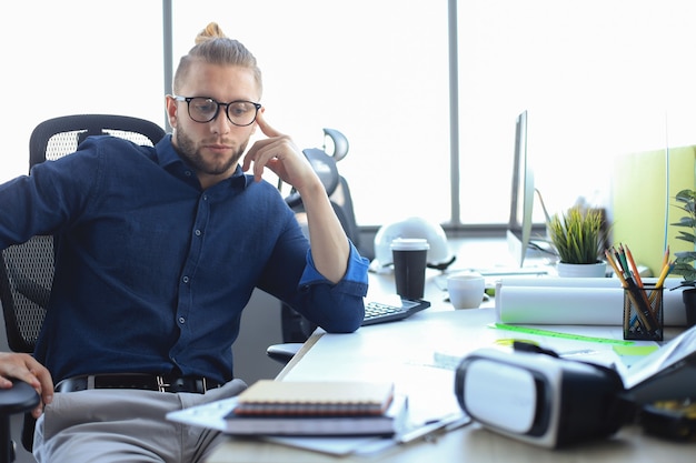 Foto moderno giovane uomo d'affari che guarda l'obbiettivo mentre è seduto in ufficio.