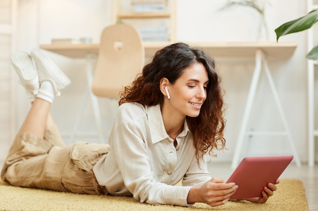 Modern young businesswoman lying on floor while listening to her coworkers during online conference