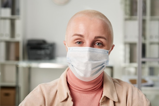 Modern young caucasian businesswoman with bald head wearing\
mask in office to protect heself against