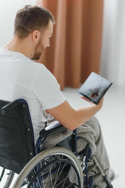 Modern young disabled man in wheelchair having video call