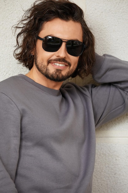 Modern young man in sunglasses with long hair, handsome man in glasses on the background of the wall, smiling, lifstyle.