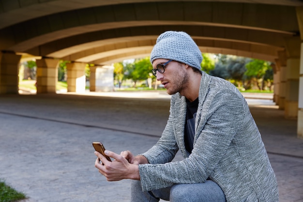 橋の下のスマートフォンを持つ現代の若い男