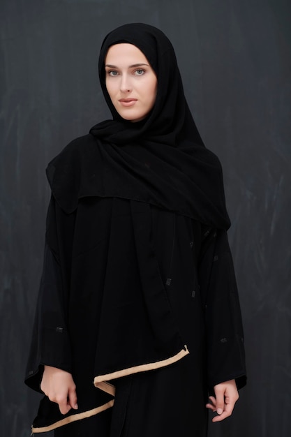 黒いアバヤを着た現代の若いイスラム教徒の女性。伝統的な服を着て、黒い黒板の前でポーズをとるアラブの女の子。モダンで豊かなアラビアのライフスタイルを代表する