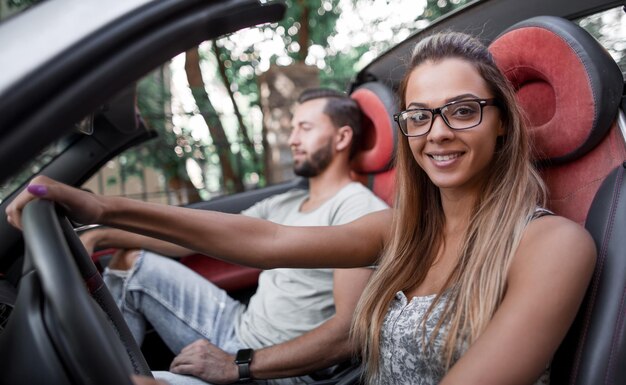 コンバーチブル車のハンドルの後ろに座っている現代の若い女性は一緒に旅行します