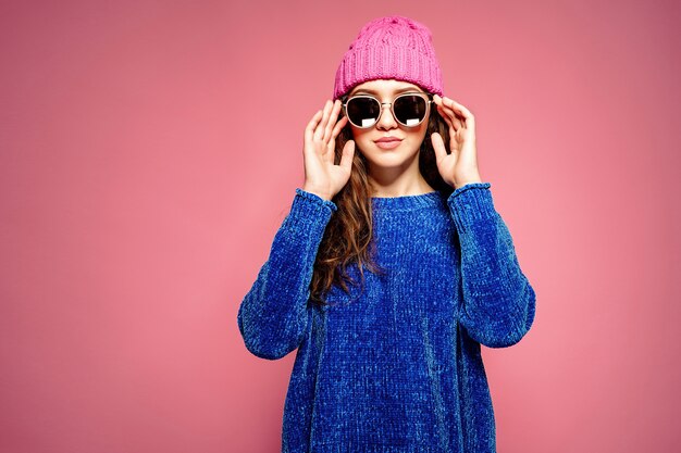 Modern young woman wearing blue sweater and pink hat posing, making funny facial expression.