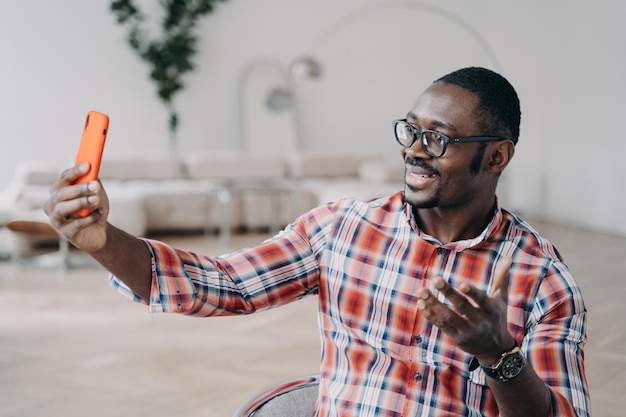 Moderne Afro-Amerikaanse man blogger in bril met smartphone online praten via video-oproep