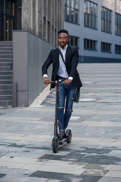 Moderne Afro-Amerikaanse zakenman rijdt elektrische scooter na het beëindigen van zijn werkdag op