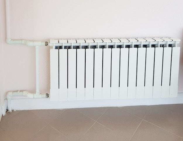 Moderne aluminium witte verwarmingsradiator op de achtergrond van een muur in een woonwijk.