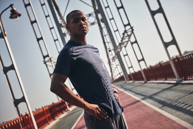 Moderne atleet. Knappe jonge Afrikaanse man in sportkleding die naar de camera kijkt terwijl hij buiten op de brug staat