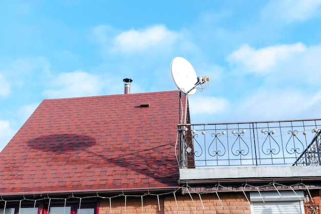 Moderne bakstenen privéwoning met rode dakspaanpannen op het dak schotelantennes open balkon op heldere blauwe lucht onderaanzicht Onroerend goed concept Draadloze televisie-uitzending ontvanger