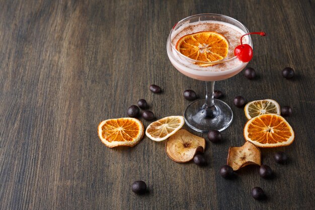 Moderne bar cocktail achtergrond. Ierse roomlikeur in champagneglas versierd met maraschino-kersen op houten tafel met assortiment van gedroogde vruchten en chocoladesnacks, kopieer ruimte