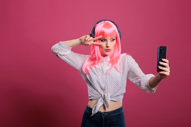 Moderne coole vrouw die foto's maakt met smartphone-app en naar muziek luistert, staande over roze achtergrond. Mobiele telefoon gebruiken om plezier te hebben met camerafoto's, vrolijk gelukkig model.