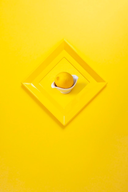 Moderne gele fotolijst op gele muur in de vorm van een diamant met een foto van een citroen