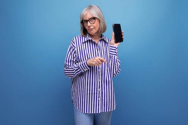 Moderne gepensioneerde vrouw van middelbare leeftijd met grijs haar bestudeert smartphonegadget op heldere studio