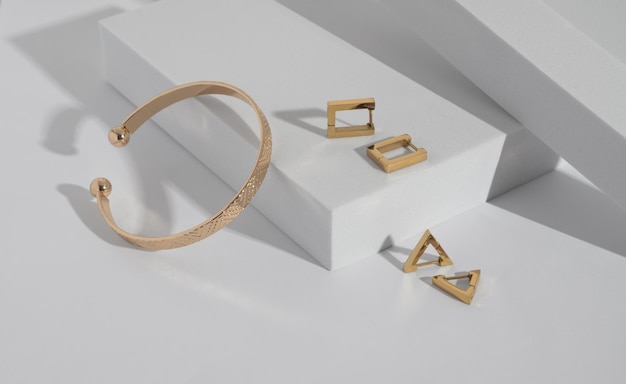 Moderne gouden armband en geometrische oorbellen op wit podium met kopieerruimte