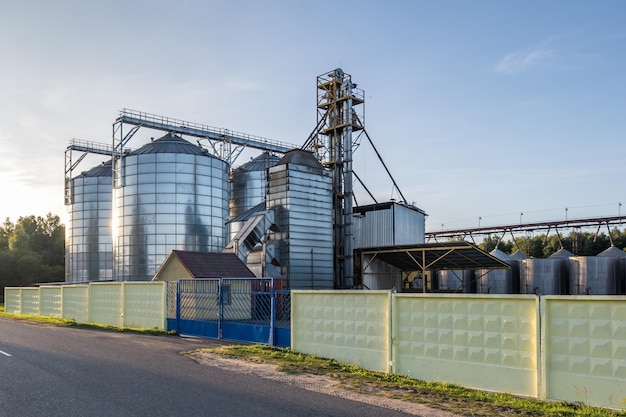 Moderne graanschuurlift met zilveren silo's op agroverwerkings- en productiefabriek voor verwerking, droogreiniging en opslag van landbouwproducten, meel, granen en graan