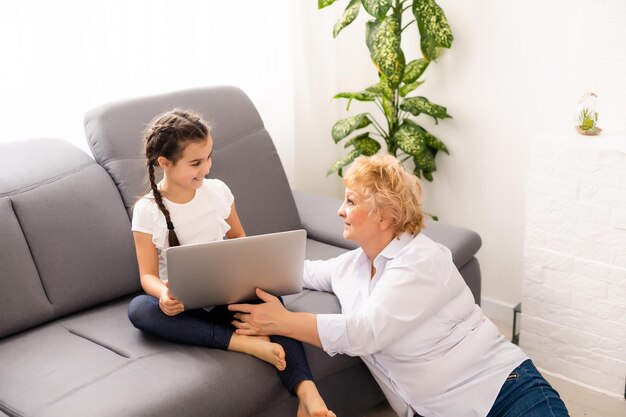 Moderne grootmoeder die kleinkind leert hoe hij een laptop thuis moet gebruiken.