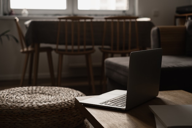 Moderne interieurinrichting. Stijlvolle lichte woonkamer ingericht met massief houten tafel, rotan poef, laptopcomputer