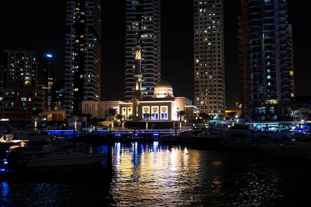 Moderne islamitische moskee verlicht door lichten omgeven door wolkenkrabbers in de jachthaven van Dubai 's nachts boten in de haven van de jachthaven van Dubai 's nachts in fel licht