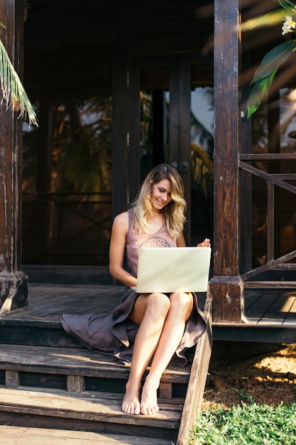 Moderne jonge vrouw werkt op laptop op vakantie in de tropen. Recreatie en toerisme. Afstandswerk. Moderne technologieën. Reizen en communicatie. Jeugd en schoonheid.