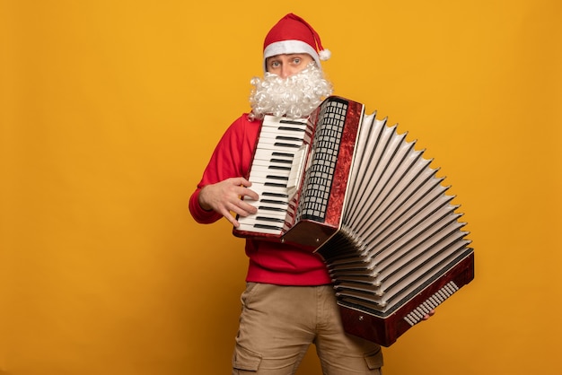 Foto moderne kerstman speelt accordeon emotioneel geïsoleerd op gele achtergrond