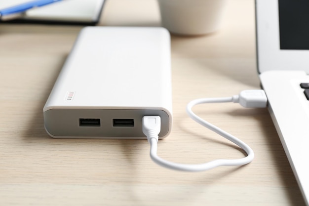 Moderne laptop opladen met powerbank op houten tafel close-up