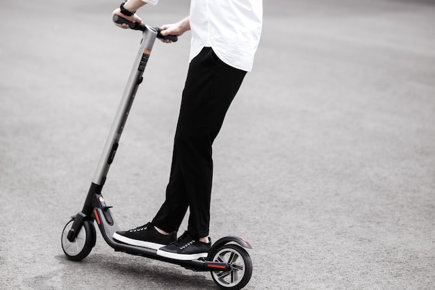 Moderne man in stijlvolle zwart-wit outfit rijden elektrische scooter in de stad.