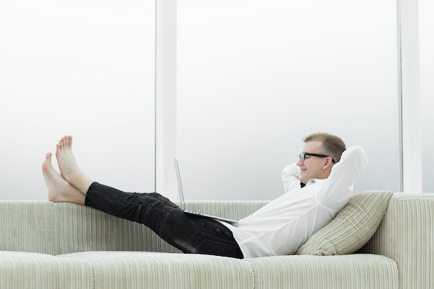 Moderne man met laptop liggend op de bank in de woonkamer
