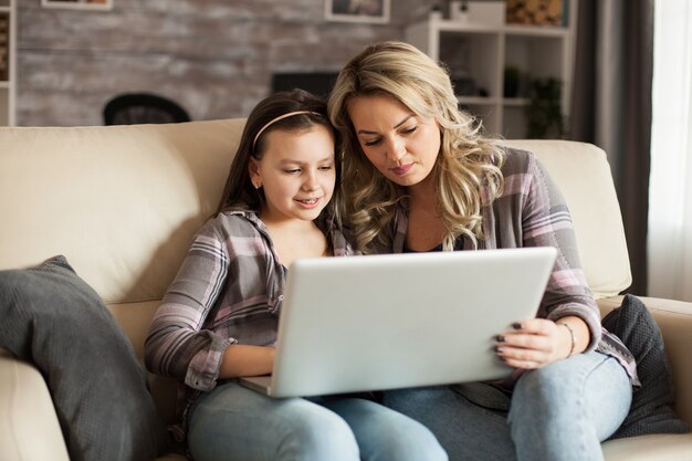 Moderne moeder en dochter zittend op de bank tijdens een lui weekend browsen op de computer.