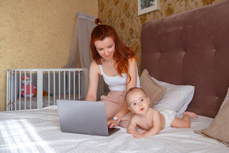 Foto moderne moeder zittend op het bed in de slaapkamer met een laptop met een baby.