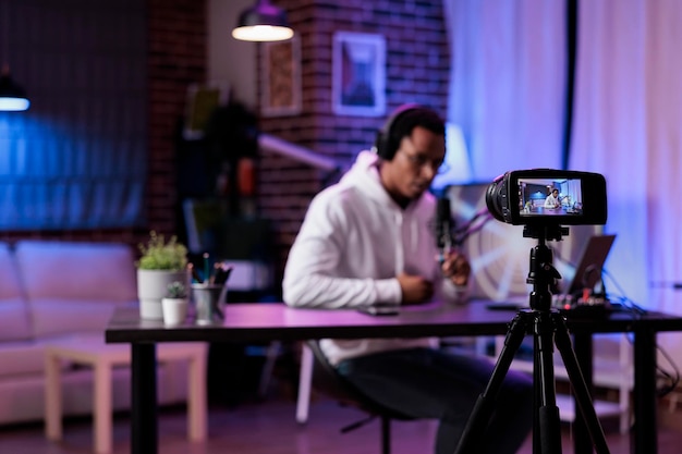 Moderne persoon die podcastaflevering filmt op camera in studio, live-uitzending online discussie om sociale media-inhoud te creëren. Mannelijke influencer vlog show met livestream apparatuur.