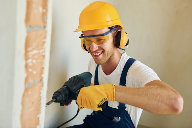 Moderne reparatie Jonge man aan het werk in uniform bij de bouw overdag