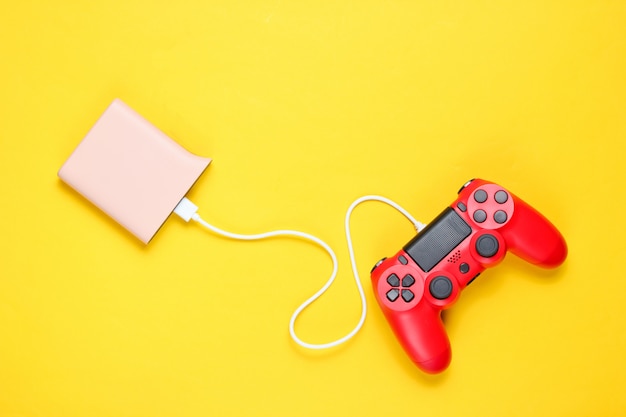 Moderne rode plastic gamepad laadt van powerbank op gele achtergrond.