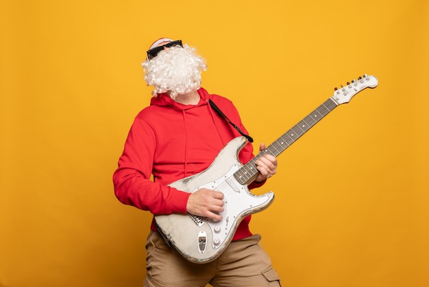 Moderne Santa Claus rock n roller gitaar spelen emotioneel geïsoleerd op gele achtergrond