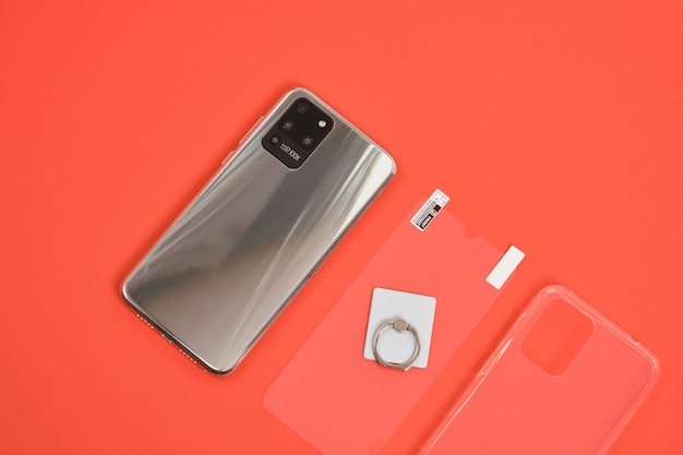 Moderne smartphone met 3 camera's met metalen behuizing, beschermend glas, ringhouder en transparante siliconen hoes op een rode achtergrond bovenaanzicht kopieerruimte hd camera 100x