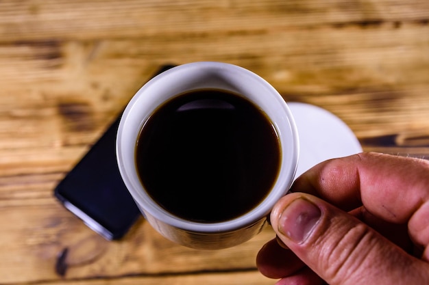 Moderne smartphone met leeg scherm op een houten achtergrond en hand met kopje koffie