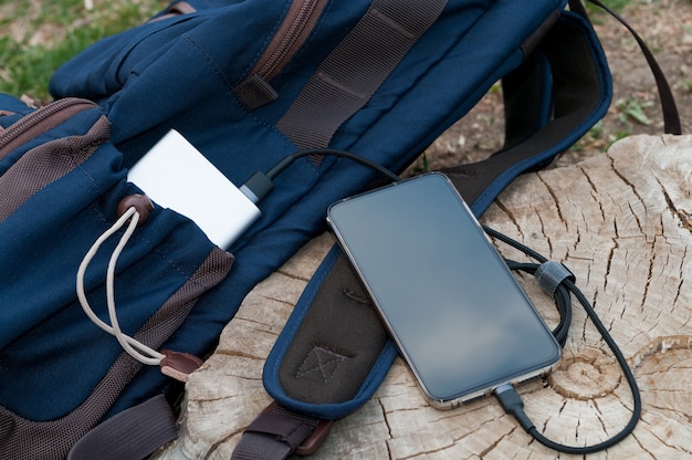 Moderne smartphone wordt opgeladen vanaf de powerbank ligt naast de rugzak op een houten stronk